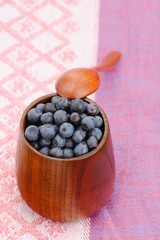 Fresh wild blueberries in wooden vase with wooden spoon on pink