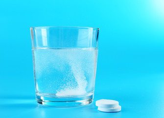 Glass of water and pills on blue background