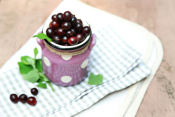 Red gooseberry in pail on wooden table close-up outdoors