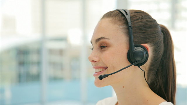 Tilt up shot of young customer service executive wearing headphones. Call center representative is communicating. Young female professional is in brightly lit office.