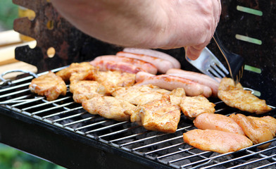 Man prepares chicken meat and sausages on grill