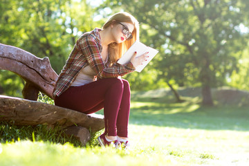 Naklejka premium Young woman sitting on a bench in the park and reading book