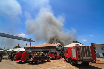 Naklejka na ściany i meble Fire truck and burning warehouses with black smoke against blue