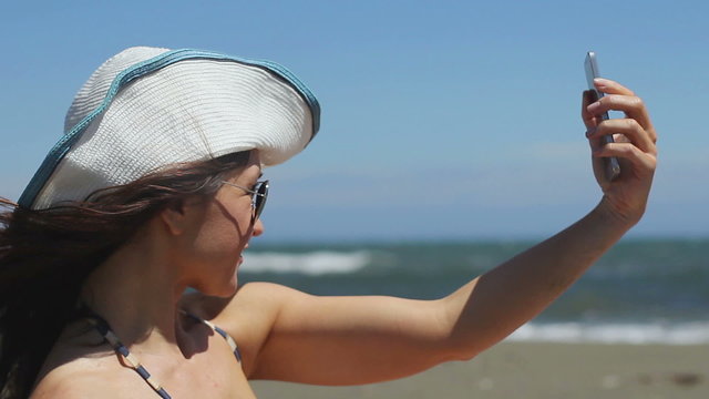 Happy beautiful female making selfie on smartphone at seaside, social networks