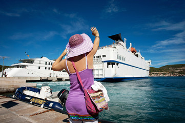Woman with a hat waving goodbye to the ship leaving the harbour
