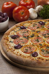 Tasty pizza, tomatoes and others ingredients on a wooden backgro