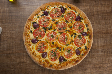 Tasty pizza, tomatoes and others ingredients on a wooden backgro
