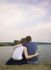 Naklejka na ściany i meble Couple hugging, sitting at river coast.