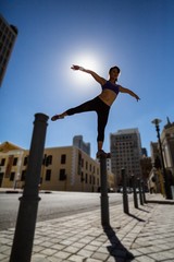 Athletic woman balancing on bollard and stretching out her arms 