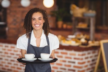 Smiling barista holding a tray of coffee cups - obrazy, fototapety, plakaty