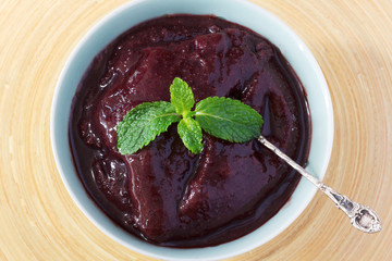 Brazilian dessert Acai pulp in blue bowl with fresh mint on wooden table. Selective focus