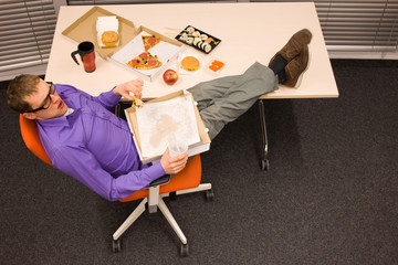 lunch in office - man sitting  with feet on the table, suffering from overeating