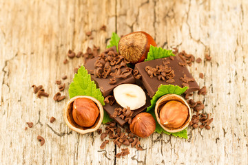 hazelnut with chocolate bars and green leaves on old wooden background
