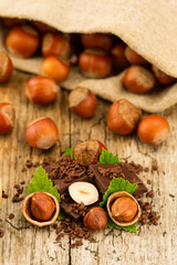 hazelnut with chocolate bars and green leaves on old wooden background