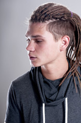 Portrait of serious man with dreadlocks and wearing a hood over gray background.
