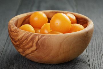 yellow cherry tomatoes in olive bowl on wood table