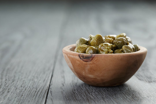 marinated capers in olive bowl on wood table with copy space
