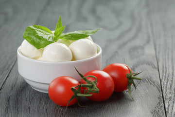 small mozzarella balls in white bowl with plum tomatoes
