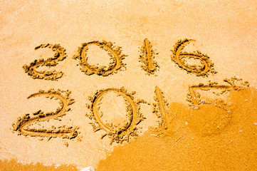 New Year 2016 is coming concept - inscription 2015 and 2016 on a beach sand, the wave is starting to cover the digits 2015