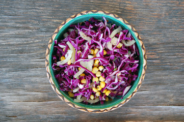 fresh red cabbage salad with sweet corn in ceramic bowl on rustic wooden table
