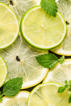 Sliced lemon, lime and mint leaves on a dark background, top vie