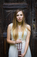 Beautiful blonde girl playing guitar in white dress