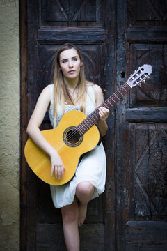 Beautiful blonde girl playing guitar in white dress