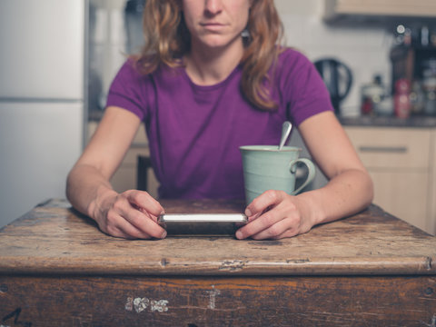 Young woman in kitchen with tea and smart phone