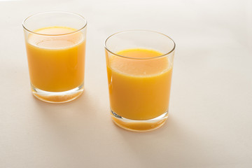 two glasses of orange juice on beige fabric background