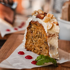 Slice of vanilla iced nut carrot cake served with afternoon tea in restaurant. Typical regional cuisine, Cape Province, South Africa. Amber tones, selective focus, low key.