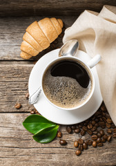 Close-up of coffee cup with roasted coffee beans on wooden background.