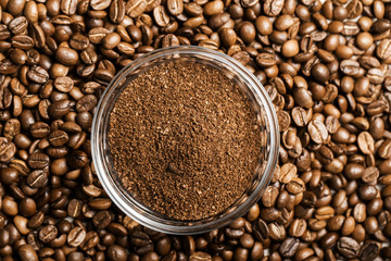 Natural ground coffee heap in transparent glass bowl on сoffee grains background
