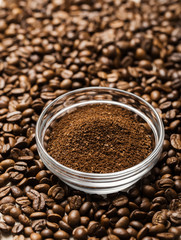 Natural ground coffee heap in transparent glass bowl on сoffee grains background