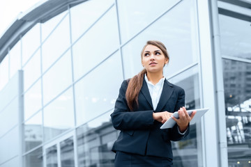 Successful businesswoman or entrepreneur using a digital tablet computer, standing in front of his office.