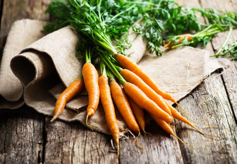 Raw carrot with green leaves  on sackcloth and wooden background