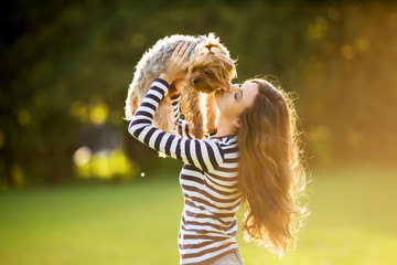 Beautiful girl in a striped sweater smiles and holds a small dog