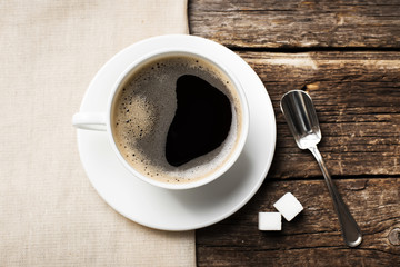 Close-up of coffee cup with roasted coffee beans on wooden background.
