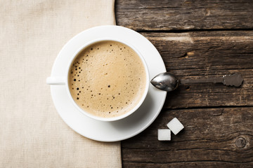 Close-up of coffee cup with roasted coffee beans on wooden background, view from the top