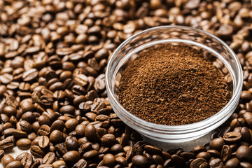 Natural ground coffee heap in transparent glass bowl on сoffee grains background