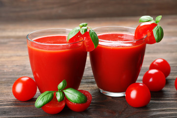 Glasses of tomato juice with vegetables on wooden background