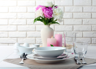 Beautiful table setting with flowers in vase on brick wall background