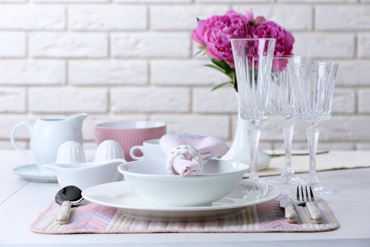 Beautiful table setting with flowers in vase on brick wall background