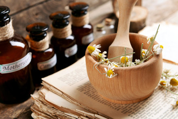 Old book with dry flowers in mortar and bottles on table close up