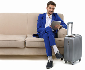 Business man with suitcase and tablet sitting on sofa isolated on white