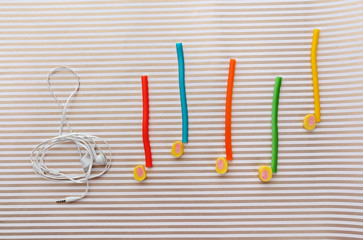 Treble clef with musical notes of candies and headphones on striped background