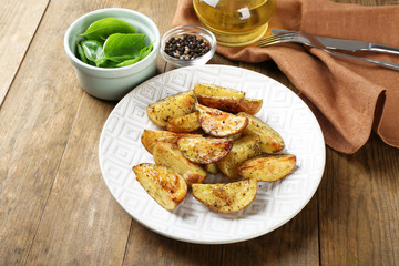Baked spicy potatoes in white plate on wooden table, closeup