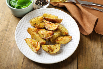 Baked spicy potatoes in white plate on wooden table, closeup