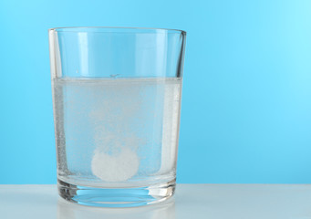 Pill in glass of water on blue background