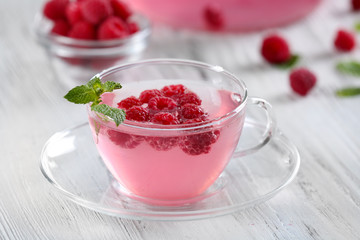 Cup and teapot of raspberry drink with berries on wooden table close up