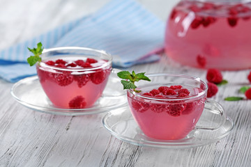 Cups and teapot of raspberry drink with berries on wooden table close up